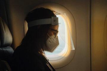 Mann mit Maske auf Reise im Flugzeug